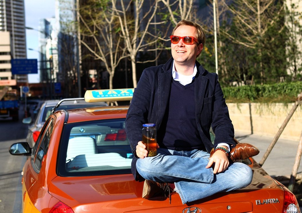 Perry sitting on a Beijing taxi with tea in hand