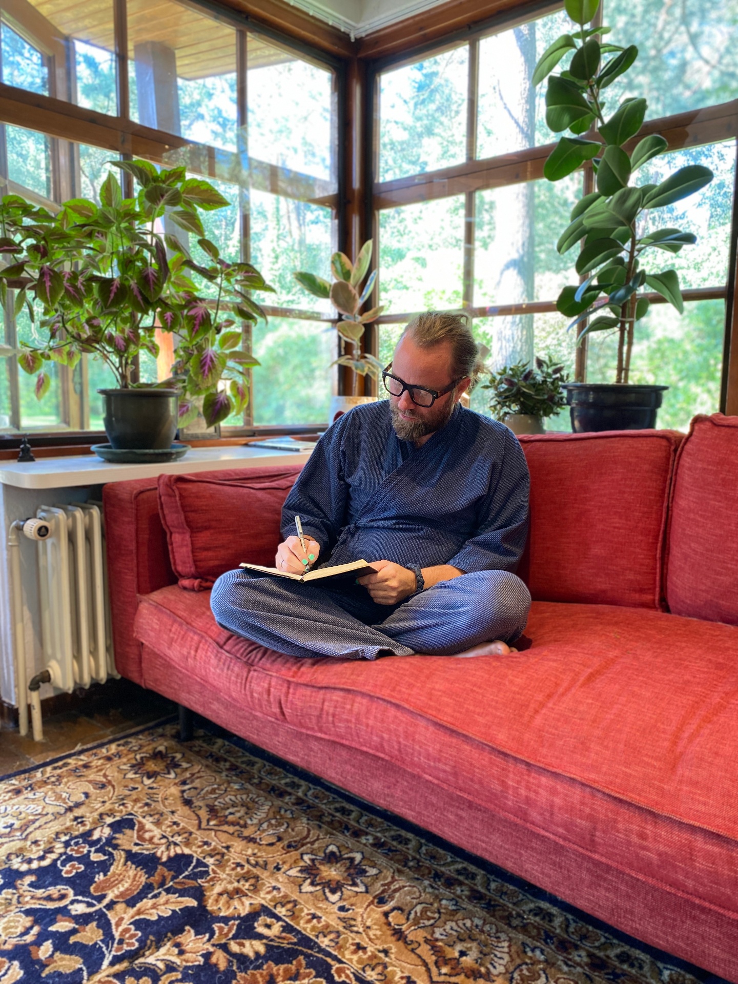 Perry writing in a notebook on a red couch surrounded by plants