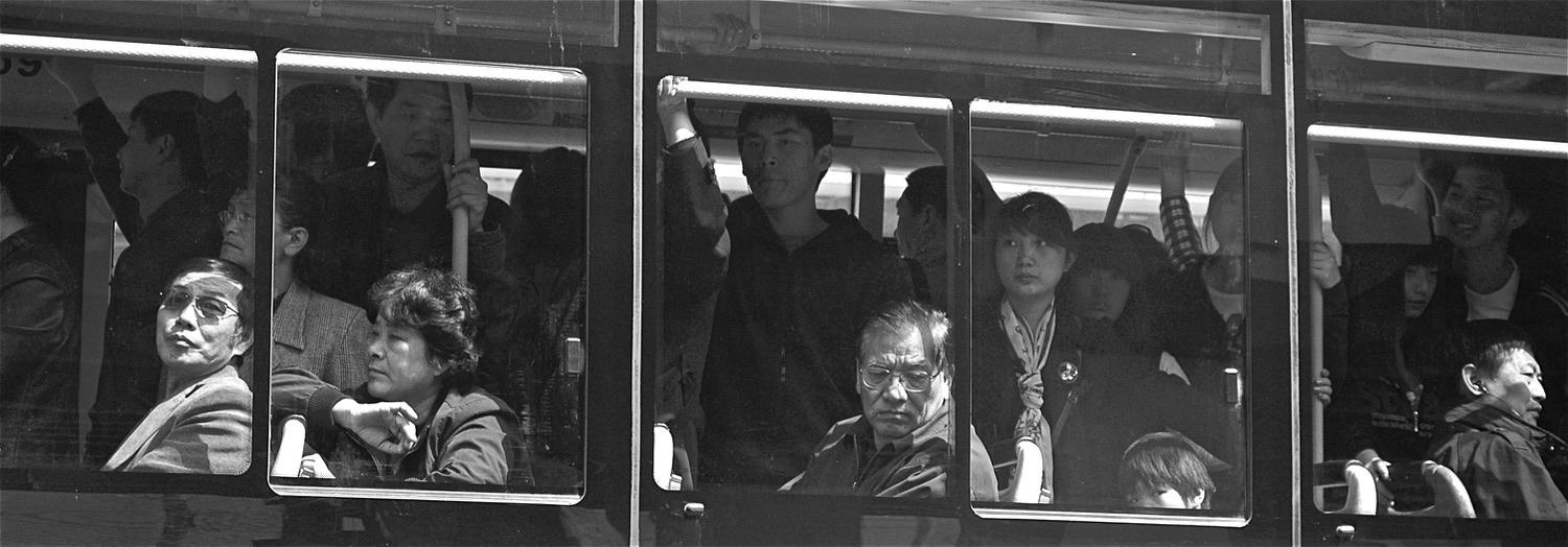 Black and white photograph of commuters seen through tram windows